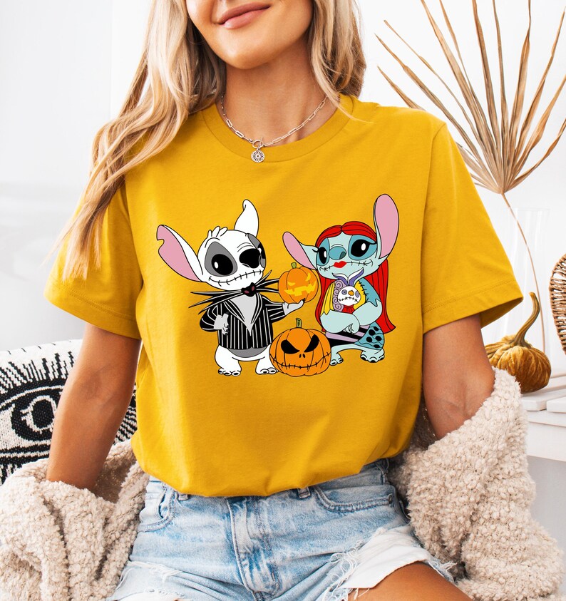 May include: Mustard yellow t-shirt with a Halloween graphic. The graphic shows two cartoon characters, one like Jack Skellington and the other Stitch, holding pumpkins. The Jack Skellington character is in a black and white striped suit.