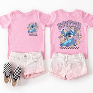 A pink t-shirt with a cartoon character and the word "STITCH" printed on it, along with a pair of white shorts and checkered shoes.