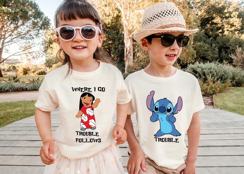 Two children wearing white t-shirts with cartoon characters and text printed on them.