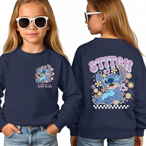 A young girl wearing a navy blue sweatshirt with a cartoon character and the name "Sophia" printed on it.
