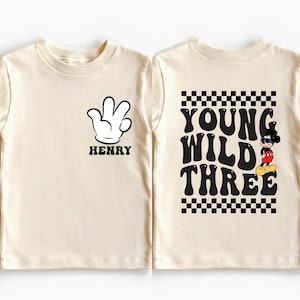 May include: Cream-colored toddler t-shirt with a black and white Mickey Mouse glove graphic and the name "HENRY" printed below it. The back of the shirt features the text "YOUNG WILD THREE" with a Mickey Mouse graphic.