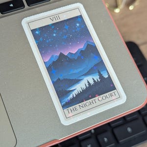 May include: A sticker with a blue and purple mountain landscape with stars and the text "VIII THE NIGHT COURT" on a laptop.
