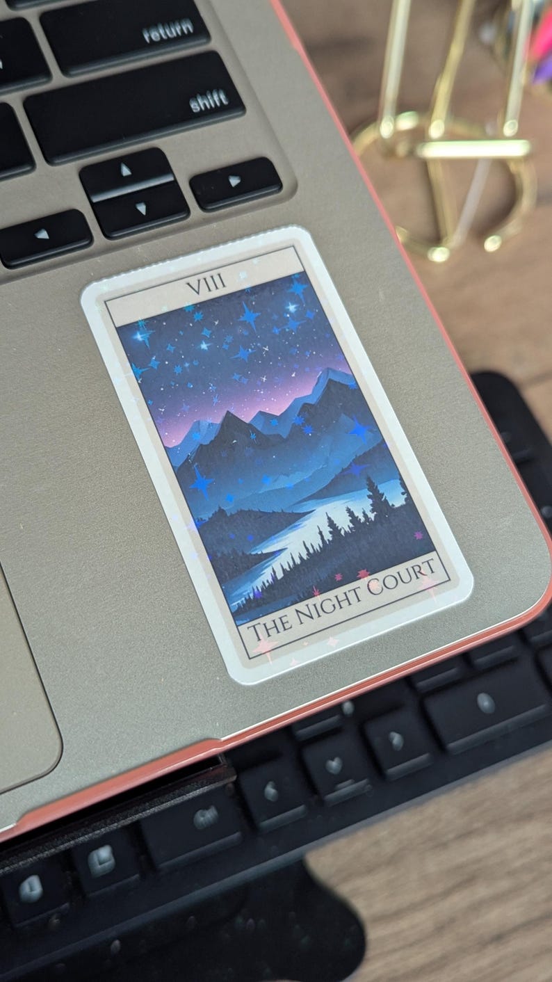 May include: A sticker with a blue and purple mountain landscape with stars and the text "VIII THE NIGHT COURT" on a laptop.
