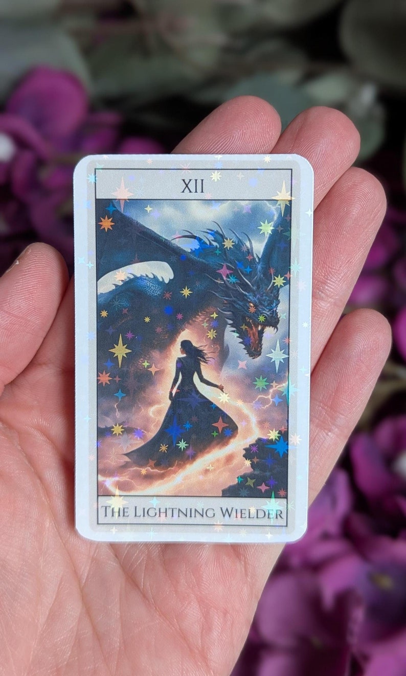 May include: A tarot card with a white background and a holographic finish. The card depicts a woman standing in front of a large, blue dragon with a lightning bolt behind them. The card number XII and the text "The Lightning Wielder" are printed on the card.