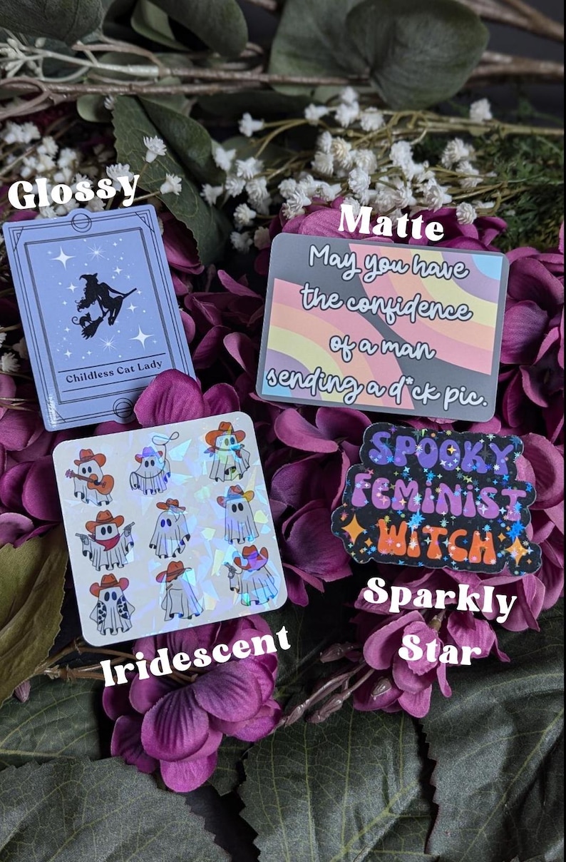 May include: A set of four stickers featuring different designs. The first sticker is glossy and features a black silhouette of a witch riding a broom with a black cat. The text "Childless Cat Lady" is printed below the image. The second sticker is matte and features a rainbow background with the text "May you have the confidence of a man sending a d*ck pic." The third sticker is iridescent and features a repeating pattern of ghosts wearing cowboy hats and holding guns. The fourth sticker is sparkly and features the text "Spooky Feminist Witch" in a rainbow font with glitter accents.