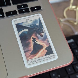 May include: A tarot card featuring a black dragon and a woman in a long dress. The card is labelled "XII THE LIGHTNING WIELDER".