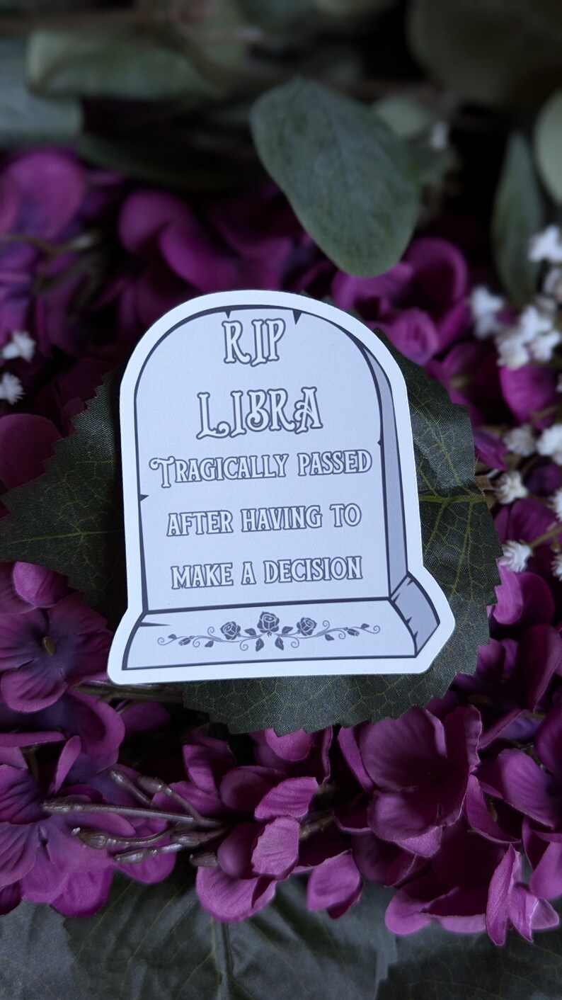May include: A white sticker with a tombstone design that reads "RIP LIBRA tragically passed after having to make a decision". The sticker is on a background of purple flowers.