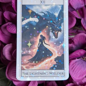 May include: A tarot card with a holographic finish depicting a woman standing in front of a blue dragon with lightning bolts. The card is labelled "XII THE LIGHTNING WIELDER".