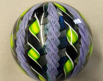 Pode incluir: Uma esfera de vidro decorativa com um acabamento brilhante. A esfera apresenta uma base preta com formas de folhas verdes e brancas e desenhos torcidos em forma de corda de cor lavanda. A esfera tem um padrão azul e verde brilhante e reflexivo.
