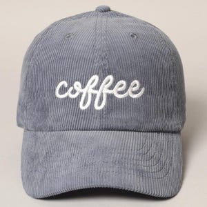 May include: A gray corduroy baseball cap with the word "coffee" embroidered in white script across the front. The cap has a curved brim and a button on top.