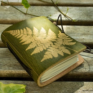 May include: A green leather journal with a gold fern design. The journal has a cork spine and a brown leather strap.