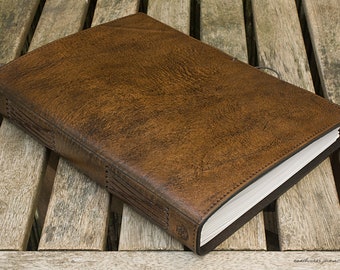 May include: A brown leather-bound journal with stitching detail on the spine. The journal is closed and lying on a wooden surface.