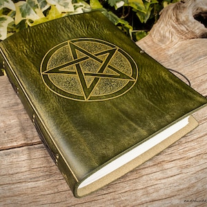 Op de afbeelding: Groen leren notitieboek met een gouden pentagram ontwerp. Het notitieboek heeft een getextureerde kaft en een touwsluiting. De pagina's zijn wit en de randen beige. Het notitieboek ligt op een houten oppervlak.