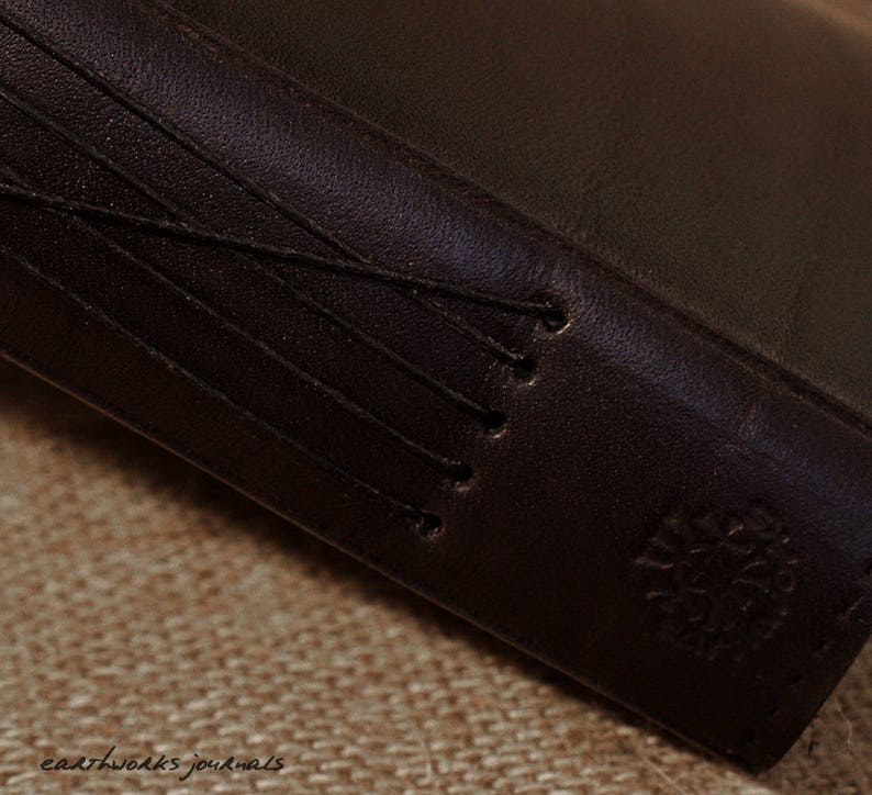 May include: Close-up of a dark brown leather-bound journal with a stitched spine and a small logo on the cover.