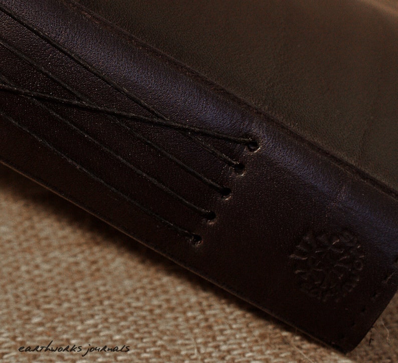 May include: Close-up of a dark brown leather-bound journal with a stitched spine and a small embossed logo on the cover.
