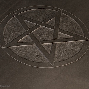 May include: A close-up of a dark brown leather journal with a five-pointed star embossed in the center.