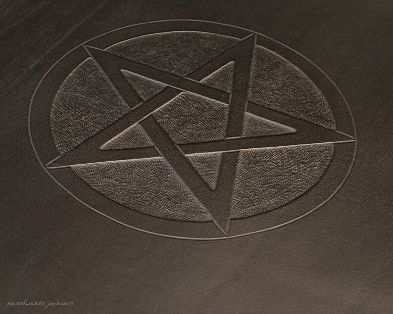 May include: A close-up of a dark brown leather journal with a five-pointed star embossed in the center.