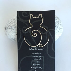 May include: Silver wire cat bookmark on a black background with the text "Mark your... with our Clip of All Pages." and the company name and contact information.