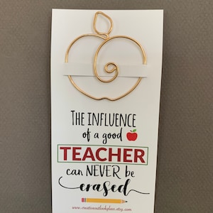 May include: A gold wire apple bookmark with the text "The influence of a good teacher can never be erased" and a website address below.