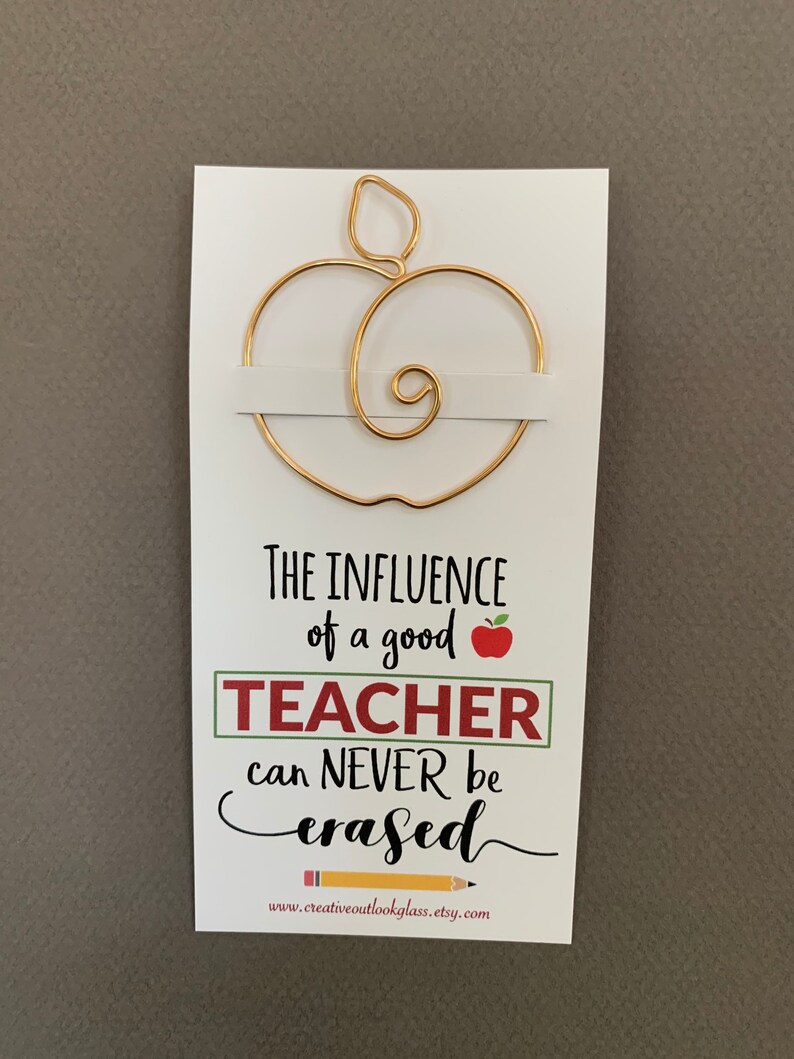 May include: A gold wire apple bookmark with the text "The influence of a good teacher can never be erased" and a website address below.