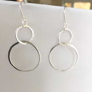 May include: Silver dangle earrings with two interlocking circles. The larger circle is hammered and has a textured finish.