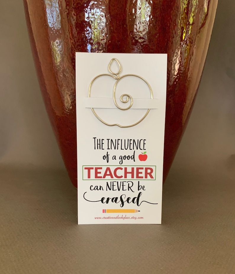 May include: A white card with a gold wire apple bookmark attached. The card reads "The influence of a good teacher can never be erased." with a red apple and a pencil graphic. The website www.creativeoutlookglass.etsy.com is printed at the bottom.