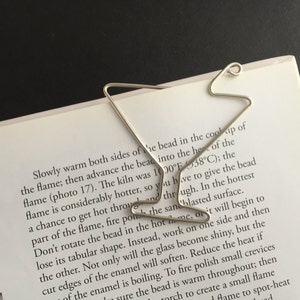 K&ouml;nnte beinhalten: Ein silbernes Lesezeichen in Form eines Martini-Glases. Das Lesezeichen liegt auf einer Seite eines Buches mit Text &uuml;ber Glasblasen.