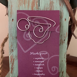 May include: A silver wire bookmark shaped like a coffee cup with the text "Mark your" and a list of genres: mystery, romance, research, recipe, fiction, and biography.