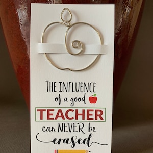May include: A white card with a gold wire apple shape on top. The card reads "The influence of a good teacher can never be erased" with a red apple and a yellow pencil graphic. The website www.creativeoutlookglass.etsy.com is printed at the bottom.