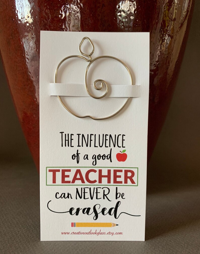 May include: A white card with a gold wire apple shape on top. The card reads "The influence of a good teacher can never be erased" with a red apple and a yellow pencil graphic. The website www.creativeoutlookglass.etsy.com is printed at the bottom.