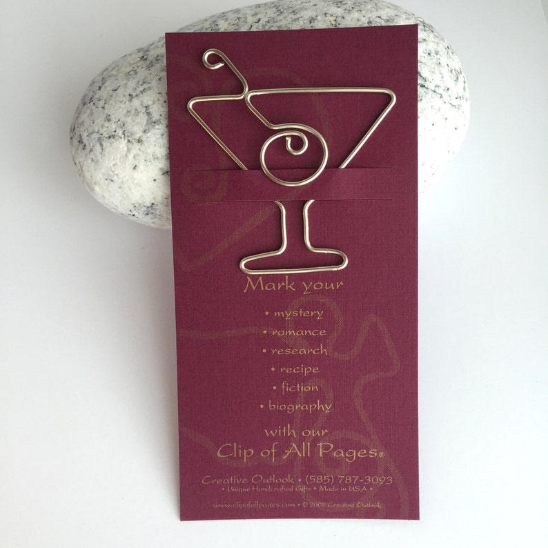 K&ouml;nnte beinhalten: Ein silbernes Lesezeichen aus Metall in Form eines Martini-Glases mit einer Olive. Das Lesezeichen befindet sich auf einer burgunderfarbenen Karte mit goldener Schrift, die "Markieren Sie Ihr Geheimnis, Romantik, Forschung, Rezept, Fiktion, Biografie mit unserem Clip of All Pages." lautet.  Creative Outlook (585) 787-3093 Einzigartige handgefertigte Geschenke Hergestellt in den USA www.creativeoutlook.com &copy; 2023 Creative Outlook