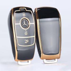 May include: Two black and gold car key covers. The key covers have a Mercedes-Benz logo and buttons.
