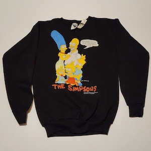 May include: Black sweatshirt featuring a graphic of The Simpsons family: Homer, Marge, Bart, Lisa, and Maggie. The design includes the show's logo and a speech bubble. The sweatshirt has long sleeves and a crew neck.