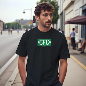 May include: Black t-shirt with a green rectangle design on the front. The design includes the letters "CFC" in white, with shamrock accents and the text "Est. 1888". The shirt is short-sleeved and appears to be made of a soft material.