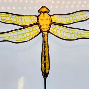 May include: A yellow dragonfly with black outlines and white accents on its wings. The dragonfly is made of glass and has a metal stem.