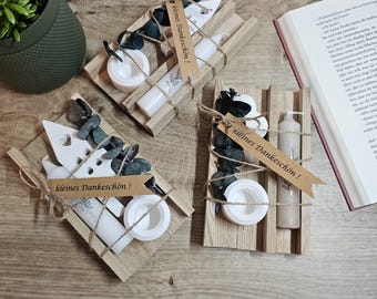May include: Three wooden gift boxes with a small candle, a tea light, and a small bottle of lotion. Each box is decorated with a small tag that says "kleines Dankeschön!" which translates to "small thank you!" in English. The boxes are tied with twine and decorated with eucalyptus leaves.