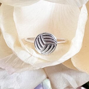 May include: A silver ring with a textured, circular design. The ring is set against a backdrop of white flower petals.