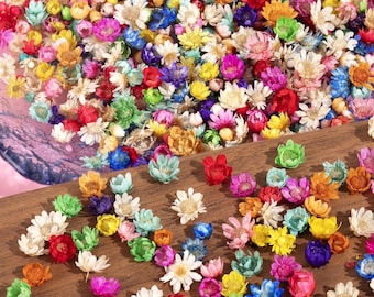 Puede incluir: Un vibrante surtido de flores secas en una variedad de colores, incluyendo rosa, amarillo, azul y naranja. Las flores están esparcidas sobre una superficie de madera, creando una exhibición colorida y texturizada. Estas pequeñas y delicadas flores son perfectas para manualidades.