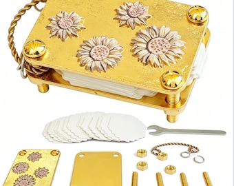 May include: A gold-toned metal flower press tool featuring a rectangular top plate with three embossed sunflower designs. The kit includes a stack of white scalloped paper inserts, a small metal wrench, four gold screws, four nuts, and a twisted metal ring.