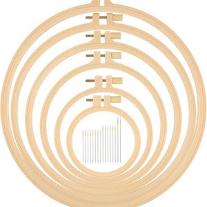 May include: A set of wooden embroidery hoops in various sizes, arranged concentrically. Each hoop has a brass-colored tightening screw. A bundle of needles is included, suggesting a craft or sewing project.