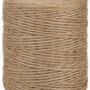 May include: A large spool of natural jute twine, tightly wound and cylindrical in shape. The twine is a light brown color, with visible fibers and a slightly rough texture. The spool has a central hole, and the twine is ready for crafting or tying.