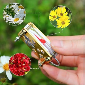 以下が含まれることがあります： クローバーのデザインが施された金色の金属製のキーホルダー。小さな透明なプラスチック製の容器に押し花が入っています。容器の中には小さな赤い花が入っています。