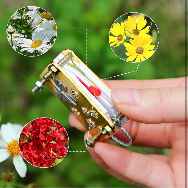 以下が含まれることがあります： クローバーのデザインが施された金色の金属製のキーホルダー。小さな透明なプラスチック製の容器に押し花が入っています。容器の中には小さな赤い花が入っています。