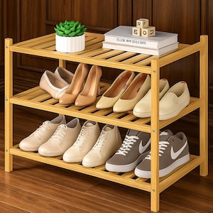 May include: A three-tiered bamboo shoe rack displaying various shoes, including heels, flats, and sneakers. The top shelf holds a small succulent in a white pot, books, and wooden letter blocks. The rack is made of light-colored bamboo.