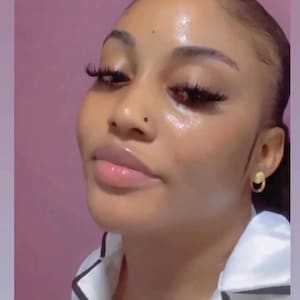 May include: A close-up of a person's face with a light complexion. They are wearing makeup, including long eyelashes and lip gloss. They have a small gold hoop earring in their right ear.