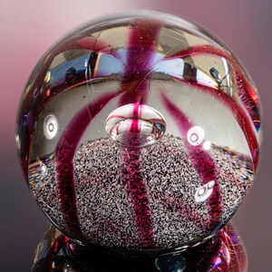 Può includere: Un fermacarte in vetro trasparente con un design rosa a spirale e uno strato di glitter argentato sul fondo.