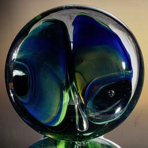 Puede incluir: Un pisapapeles de vidrio con un diseño de espiral azul, verde y amarillo. El diseño de espiral se asemeja a una mariposa.