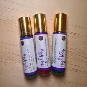 以下が含まれることがあります： 「High Vibes」とラベル付けされた、ポジティブな影響を与える明確さを促すエッセンシャルオイルブレンドの10mlロールオンボトル3本。ボトルは金色のかぶせ蓋と透明なガラス製で、中には青、ピンク、緑の液体が入っています。