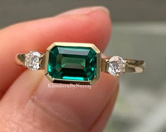 May include: A gold ring with a large emerald green gemstone and two smaller round diamonds on either side.