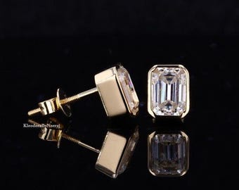 May include: A pair of gold earrings featuring emerald cut cubic zirconia stones. The earrings are set in a simple, elegant design.